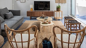 A modern living room with a grey sofa, a wooden TV stand, a round coffee table, and wicker chairs. - Piso Azul (Lisbon)
