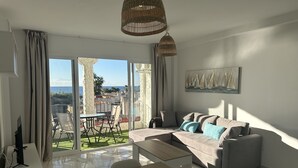 A modern living room with a large window, a sofa, a dining table, and a painting of sailboats. - Sunstay Relax 69 Rio Marina Nerja (Nerja)