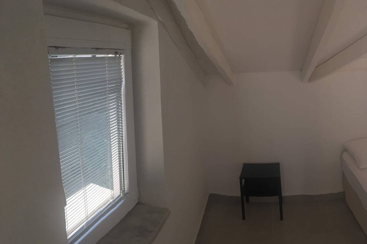 A small, single-bed room with a window, a small table, and a wardrobe.