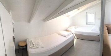 Un dormitorio pequeño con dos camas, un taburete y una ventana.