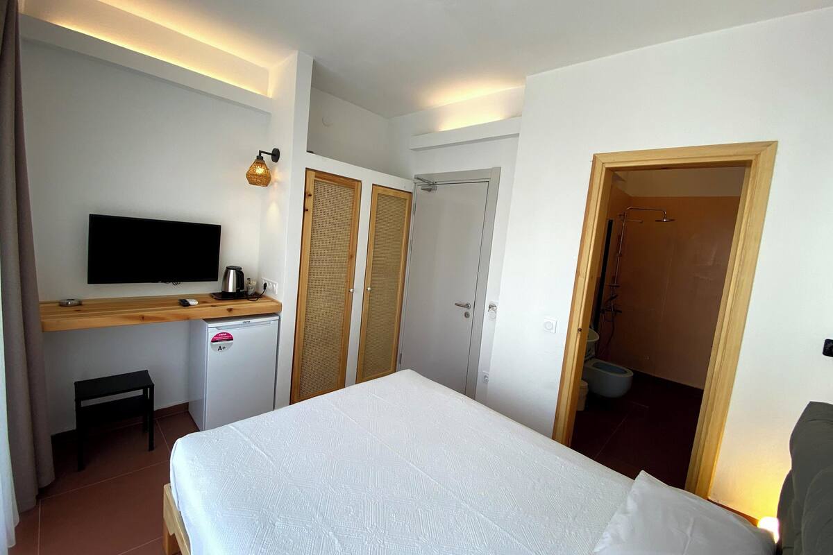 A bedroom with a bed, a TV, a small fridge, and a wooden desk.