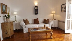 Una sala de estar con un sofá blanco, una mesa de centro de madera y un reloj en la pared.