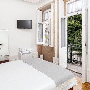 Une chambre avec un lit, une télévision, un radiateur et une fenêtre donnant sur un balcon et de la verdure.