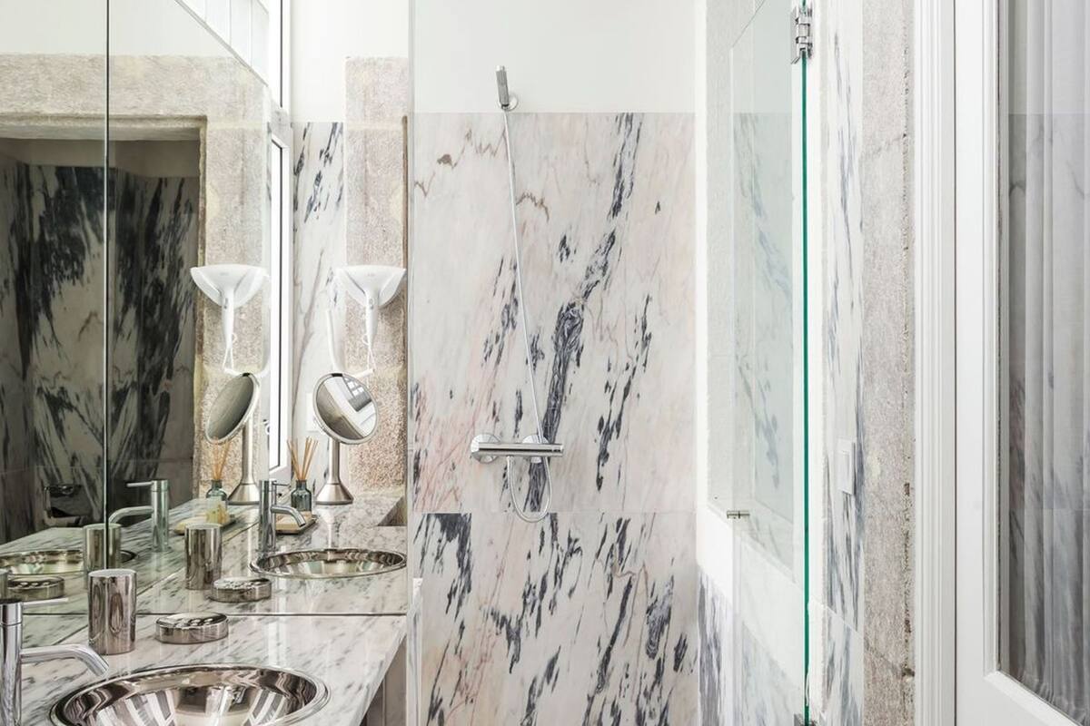 Een moderne badkamer met marmeren aanrechtbladen, een grote spiegel, een douche en een douchecabine met glazen wanden.