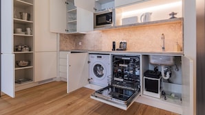 A compact kitchen with a built-in washing machine, a microwave, and a sink. - Ando Living - São Nicolau Townhouse (Lisbon)