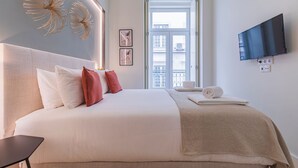 A modern hotel room with a large bed, a flat-screen TV mounted on the wall, and a window with a view of the city. - Ando Living - São Nicolau Townhouse (Lisbon)