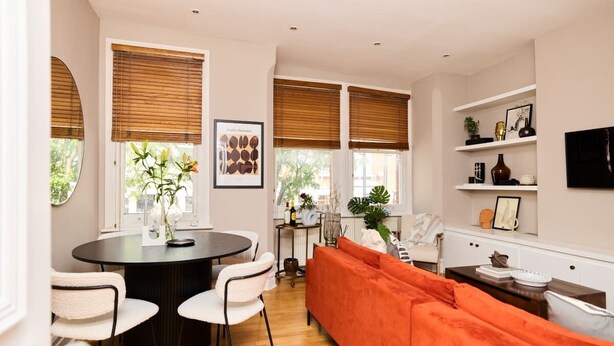 A modern living room with a round dining table, white chairs, and an orange sofa. - The Waterlow Park Wonder - Trendy 2bdr With Study Room and Patio (London)