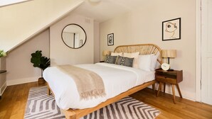 A bedroom with a sloped ceiling, a bed with a wooden frame, a round mirror, and a bedside table with a lamp. - The Waterlow Park Wonder - Trendy 2bdr With Study Room and Patio (London)