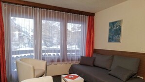 Une pièce comprenant un canapé, deux fauteuils, une petite table et une fenêtre avec des rideaux.