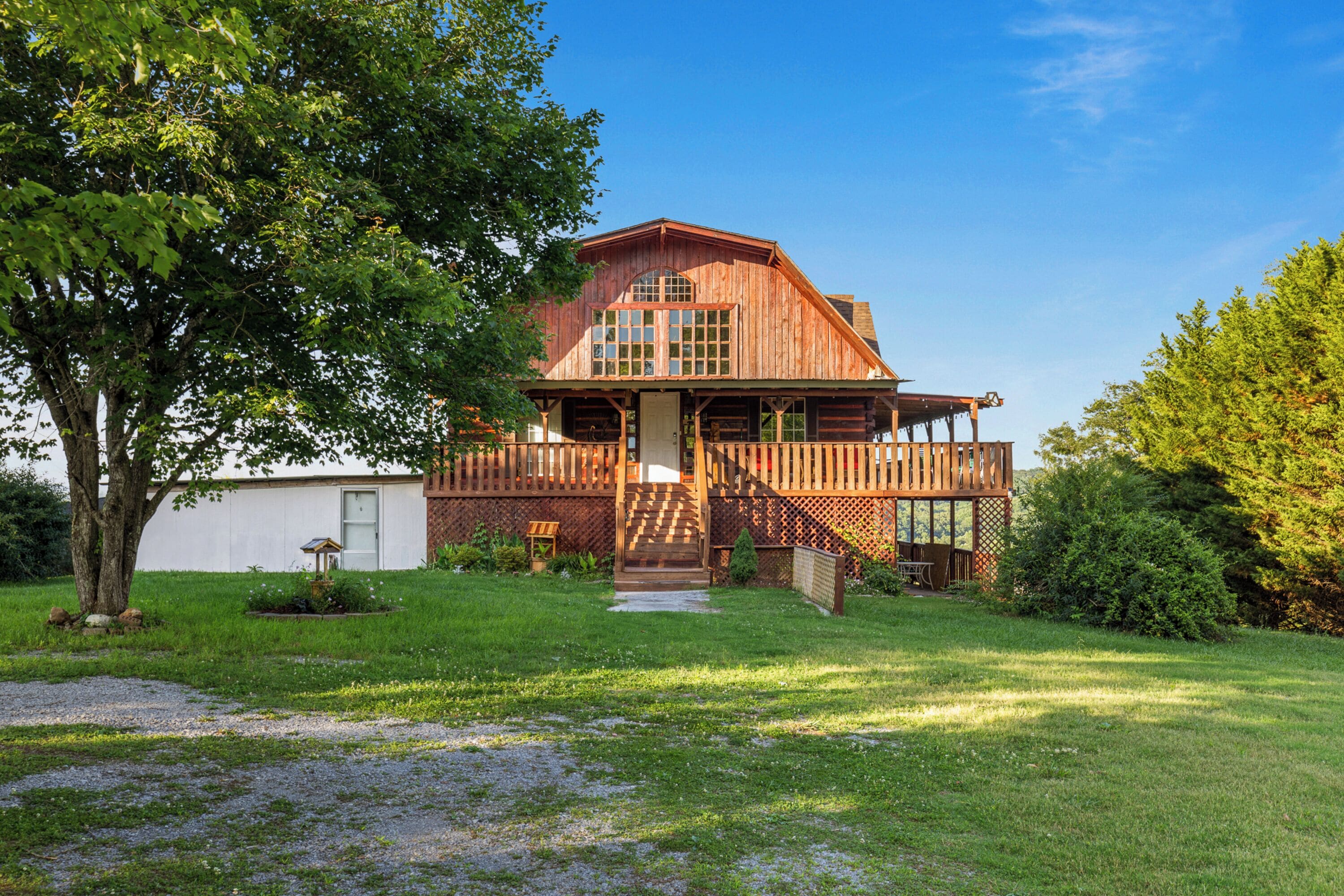 A two-story wooden house with a porch, surrounded by a well-maintained lawn and trees.