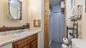 A bathroom with a wooden vanity, a sink, a mirror, and a shower enclosure.