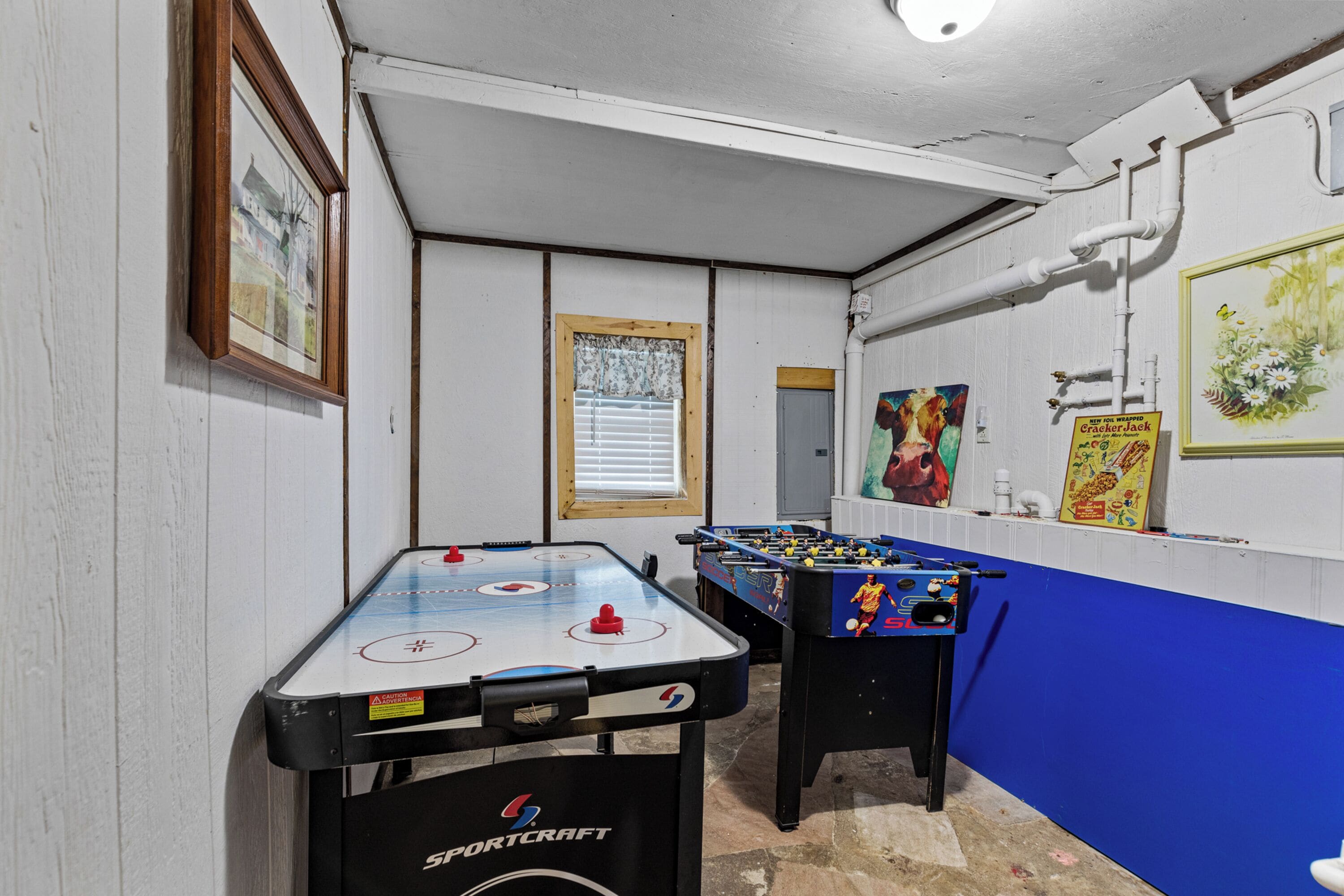 Une pièce avec deux tables de baby-foot, une fenêtre avec des stores et un mur orné de tableaux.