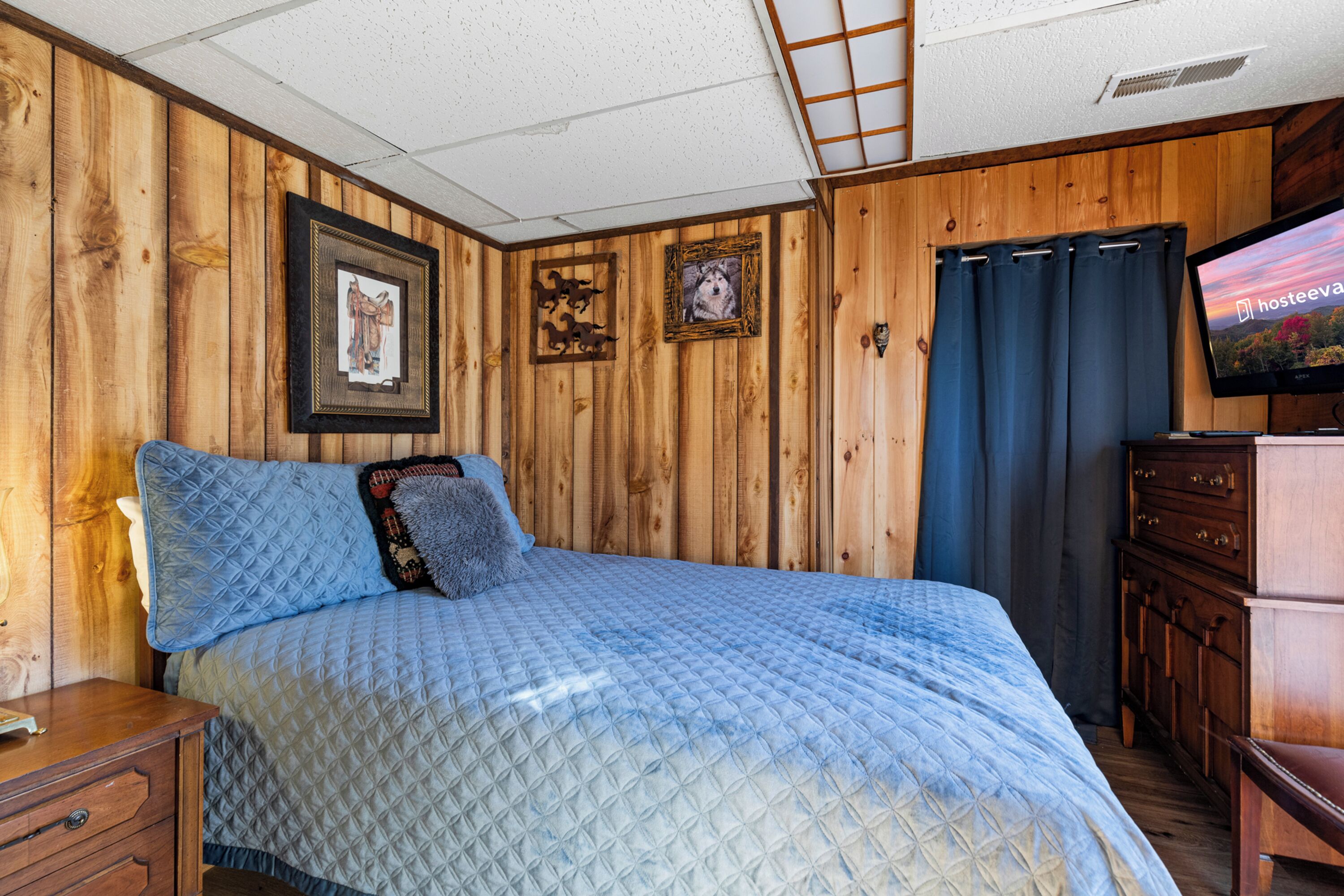 A wooden-paneled room with a bed, a TV, and a dresser.