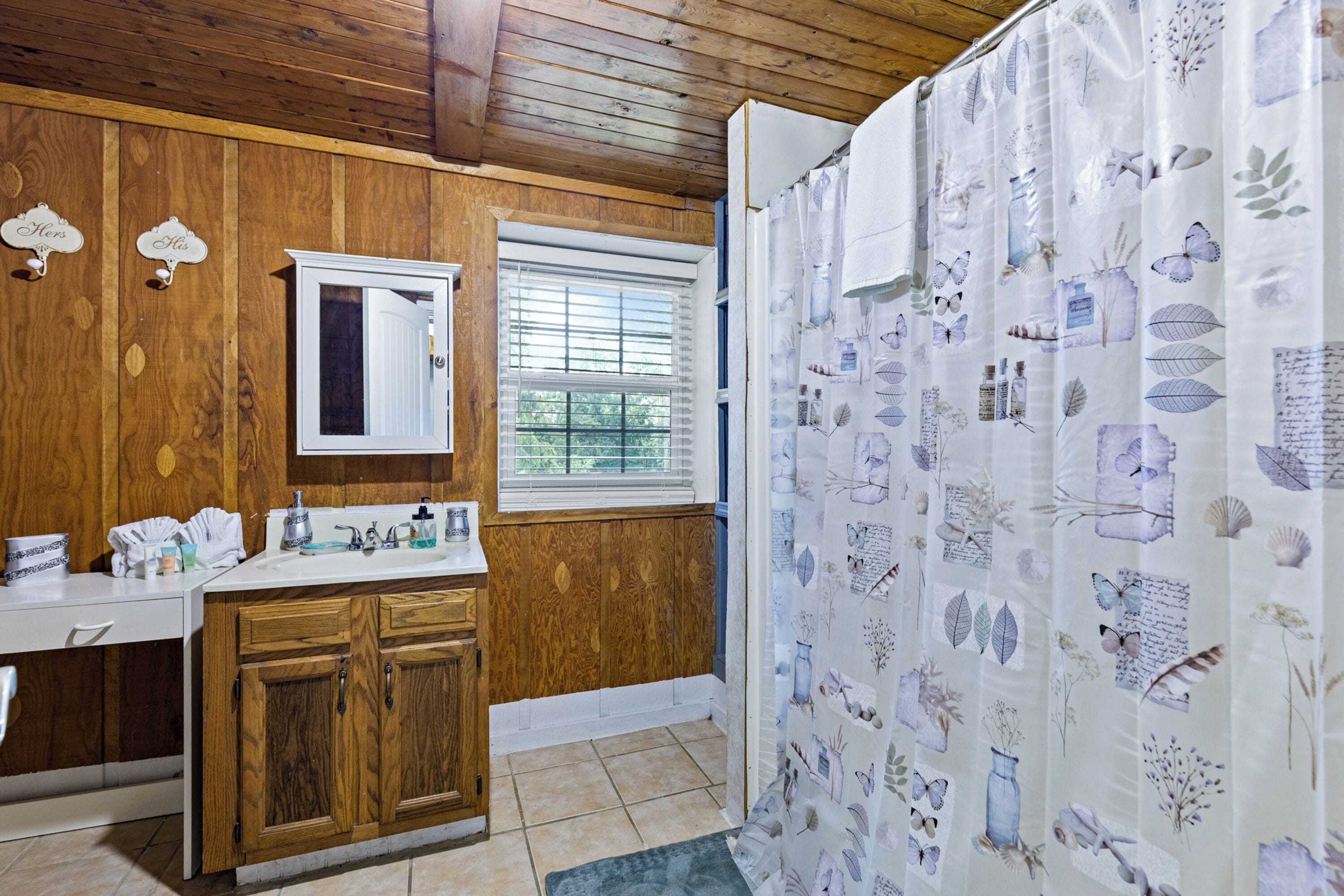 A bathroom with wooden walls, a white sink, and a window with blinds.