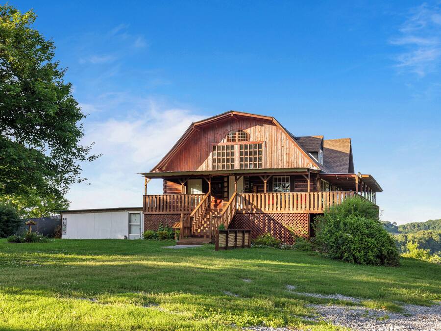 A large wooden house with a porch, a staircase, and a well-maintained lawn.