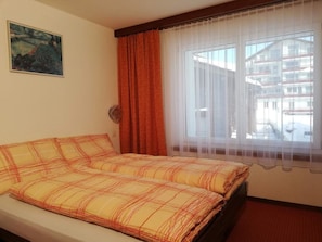 Une chambre d’hôtel avec un lit, une fenêtre avec des rideaux, un tableau au mur et une vue sur les bâtiments environnants.
