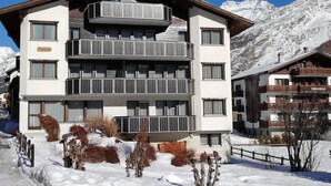 Un hotel de varios pisos con balcones, una pista de esquí al fondo y un paisaje cubierto de nieve.