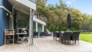 Una terraza al aire libre con una parrilla, mobiliario de mimbre y una zona cubierta con una mesa y sillas.