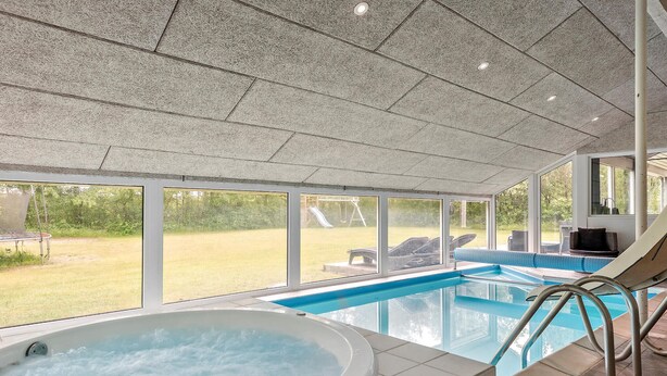 Una piscina interior con jacuzzi, ventanas amplias y vistas a un patio trasero con tobogán y mobiliario exterior.