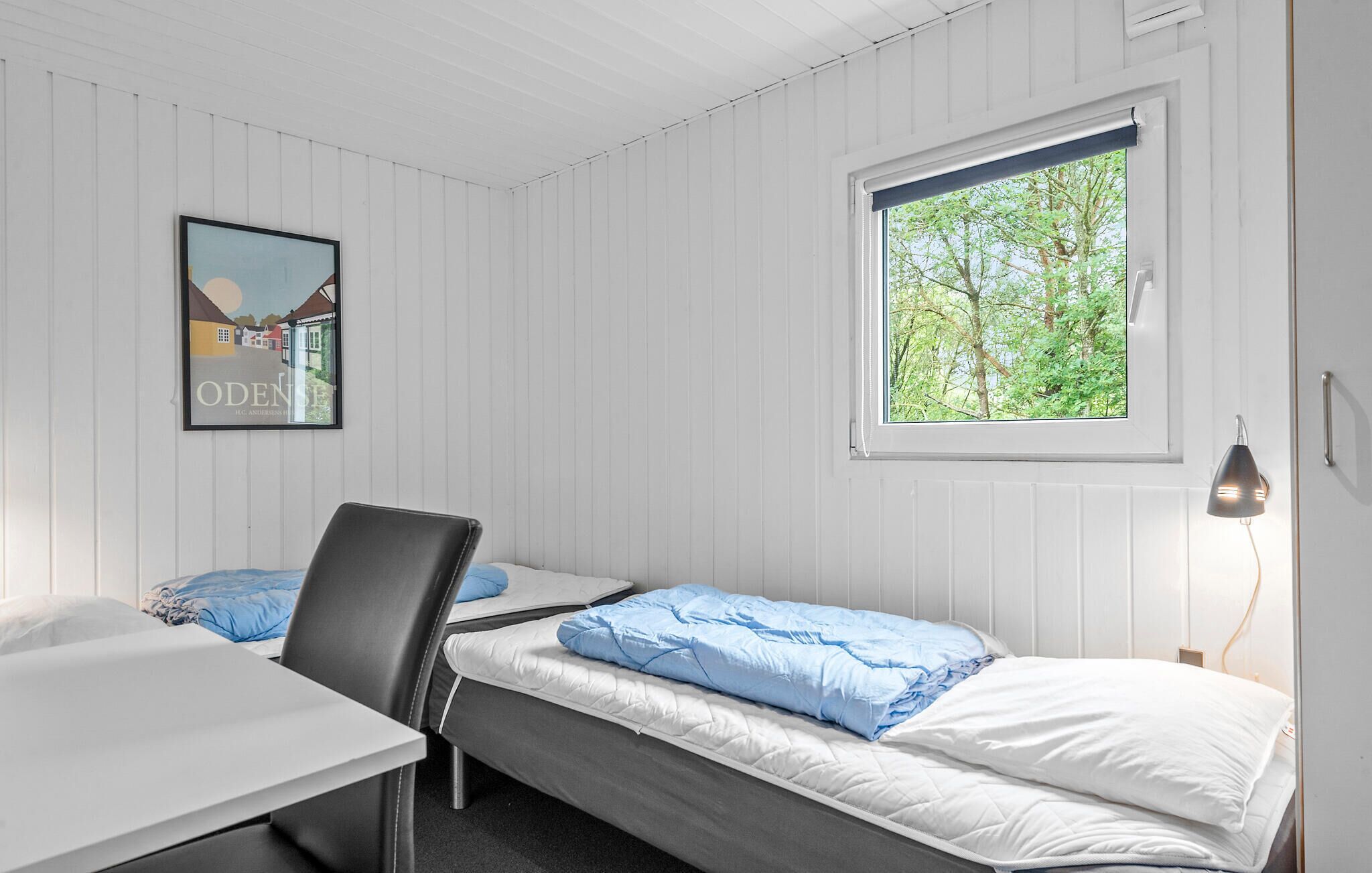 Een kamer met twee bedden, een bureau, een stoel, een raam met uitzicht op bomen en een lijst aan de muur.