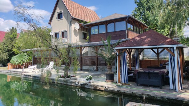 Ein zweistöckiges Haus mit rotem Ziegeldach, einer Holzterrasse und einem kleinen Teich.