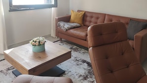 Ein Wohnzimmer mit einem braunen Ledersofa, einem Couchtisch mit floraler Dekoration, einem braunen Sessel und einem gerahmten Bild an der Wand.