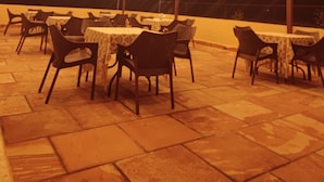 An outdoor dining area with tables and chairs, under a metal roof with hanging lights. - Jim's Inn (Ramnagar)