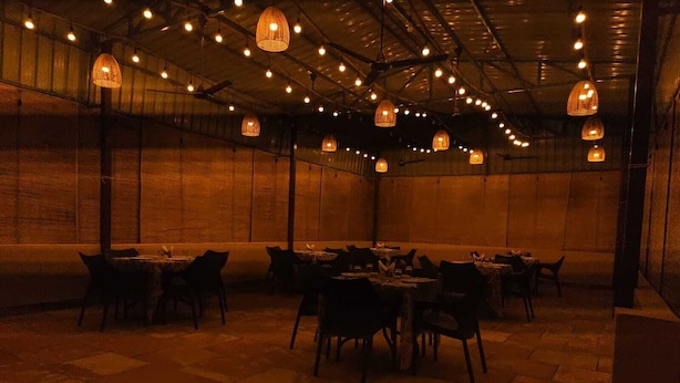A dimly lit restaurant with tables and chairs arranged in a spacious room with a high ceiling and exposed beams. - Jim's Inn (Ramnagar)