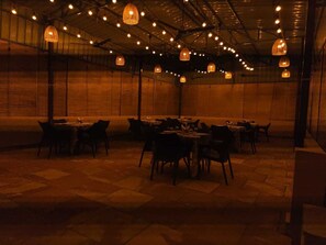 A dimly lit restaurant with tables and chairs arranged in a spacious room with a high ceiling and exposed beams. - Jim's Inn (Ramnagar)