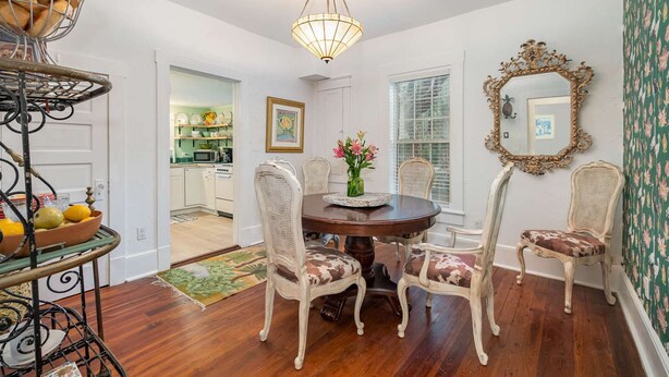 A dining room with a round table, four chairs, a chandelier, and a mirror on the wall.