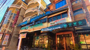 A building with multiple floors, balconies, and a variety of signs indicating different businesses including a laundry and cafe.