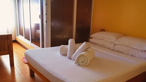 A neatly made bed with white linens and rolled towels, a wooden chair, and a sliding glass door leading to an outdoor area.
