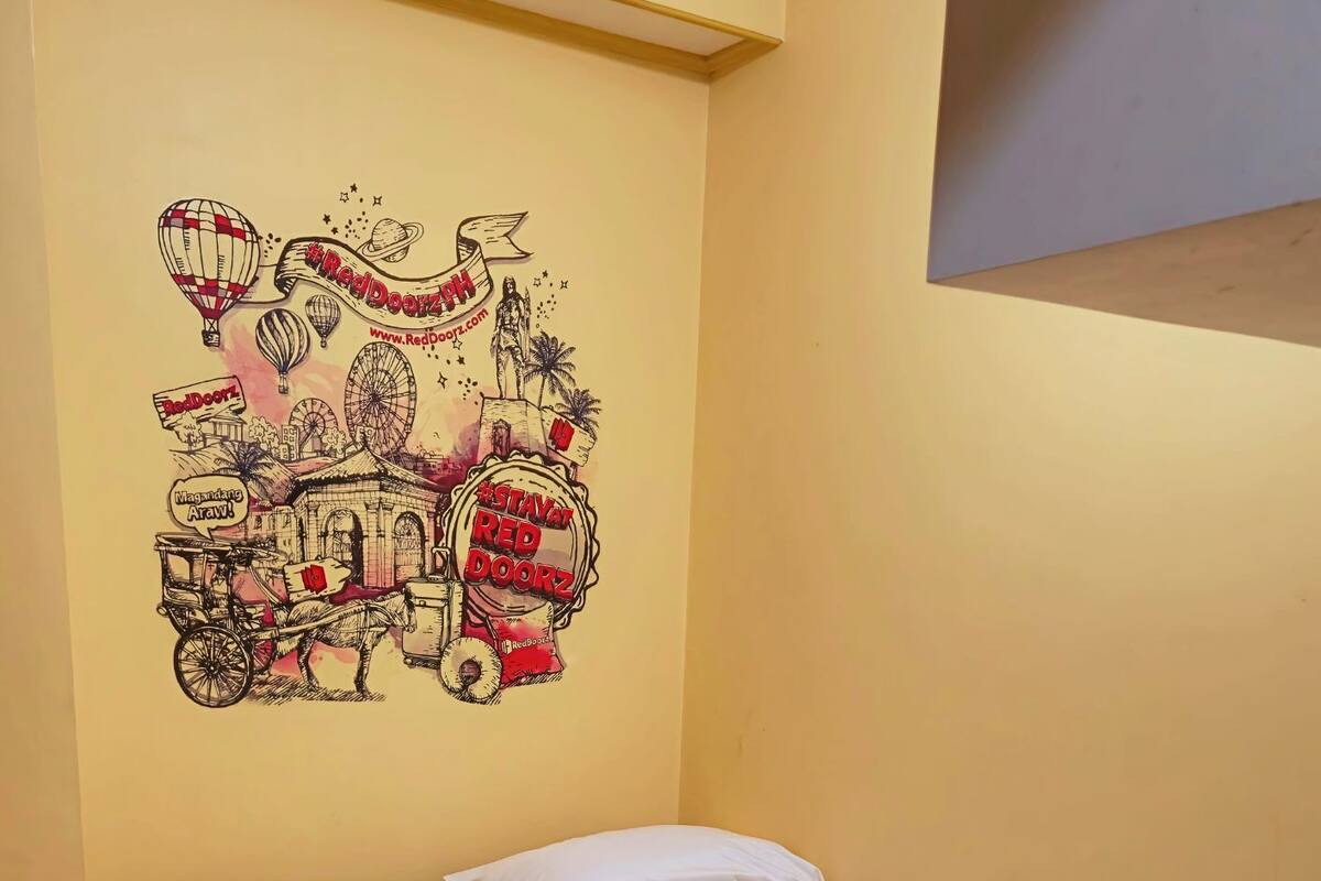 A hotel room with a bed, white pillows, and rolled towels. There is a wall mural depicting a hot air balloon, a Ferris wheel, and a building with a sign that reads "Red Door."
