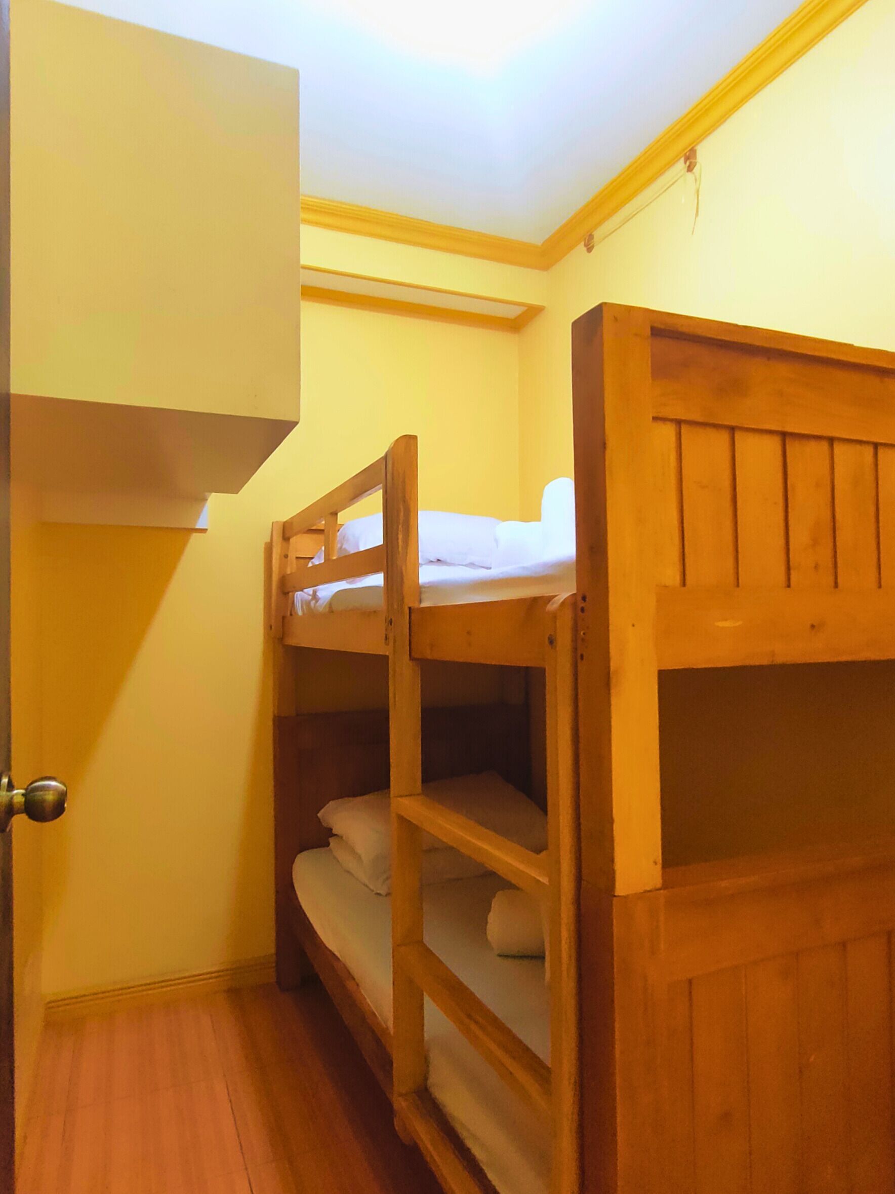 Een kleine, compacte kamer met een stapelbed en een enkel bed. Een deur aan de linkerzijde en een klein raam aan de rechterzijde.