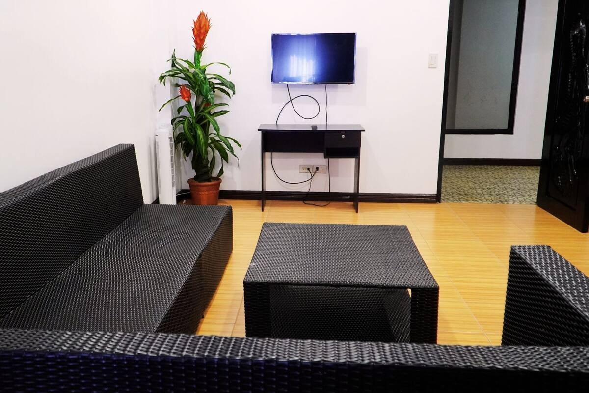 A living room with a black sofa, a small table, and a potted plant.