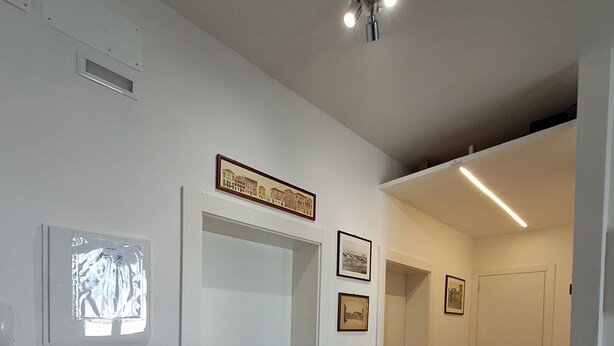 A modern interior with a wooden floor, white walls, and a ceiling light fixture. There are framed pictures on the walls and a door leading to another room. - Bubi's Apartment, Intero Appartamento di 65mq (Livorno)