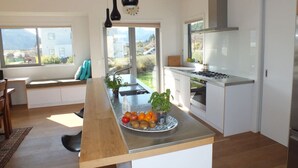 A modern kitchen with a central island, a dining area with a bench, and large windows offering a view of the outdoors.