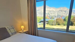 A hotel room with a large bed, a nightstand with a lamp, and a window offering a mountain view.