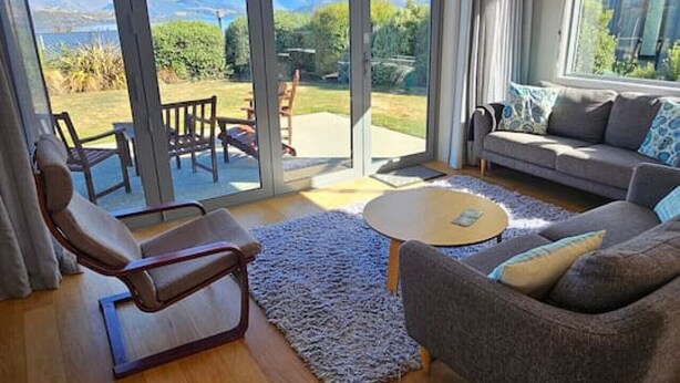 A spacious living room with a large sliding glass door leading to an outdoor area, a grey sofa, a wooden coffee table, and a lounge chair.