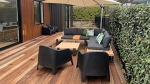 An outdoor patio with a wooden deck, black furniture, and a large umbrella. - Moments from That Wanaka Tree - only a 5-minute walk to That Wanaka Tree (Wānaka)