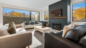 A modern living room with a fireplace, large windows, and a view of trees. - Moments from That Wanaka Tree - only a 5-minute walk to That Wanaka Tree (Wānaka)