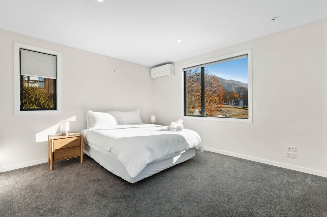 A modern bedroom with a large bed, a nightstand, a framed picture, and a window with a mountain view.