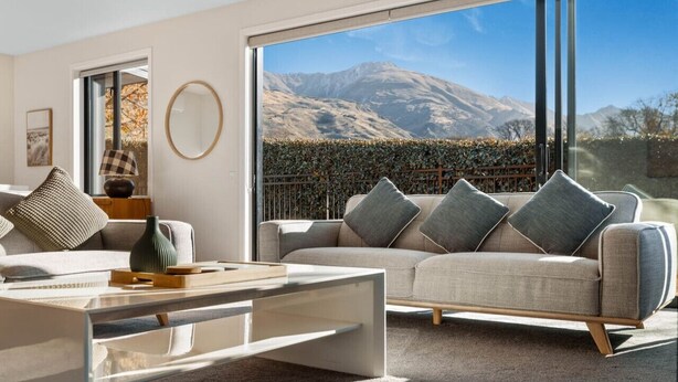 A modern living room with a sofa, coffee table, and a large window offering a mountain view. - Moments from That Wanaka Tree - only a 5-minute walk to That Wanaka Tree (Wānaka)