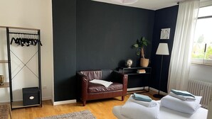 Une pièce moderne avec un mur d’accent de couleur sombre, un fauteuil en cuir, un canapé blanc, une petite table d’appoint avec une plante et un radiateur.