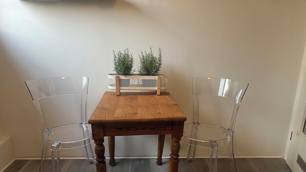 Une table en bois, quatre chaises, deux plantes en pot et un mur blanc.