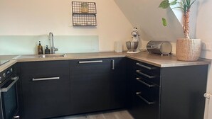 Une cuisine moderne avec des meubles de couleur noire, un plan de travail en bois, un four encastré et un petit îlot central agrémenté d’une plante.