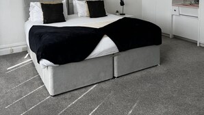 Camera da letto moderna con un letto grigio, biancheria nera e bianca, due opere d'arte incorniciate, un lampadario e un armadio bianco.