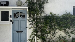 Una casa residenziale con una porta blu, un muro bianco e un piccolo giardino fiorito di fiori rossi.