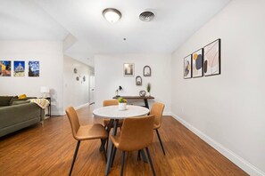 Uma sala de estar moderna com uma mesa de jantar redonda, quatro cadeiras, um sofá e obras de arte nas paredes.