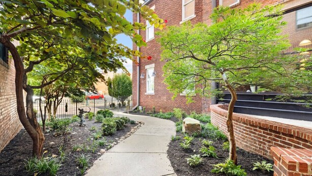 A brick building with a paved walkway, small trees, and a stone wall.